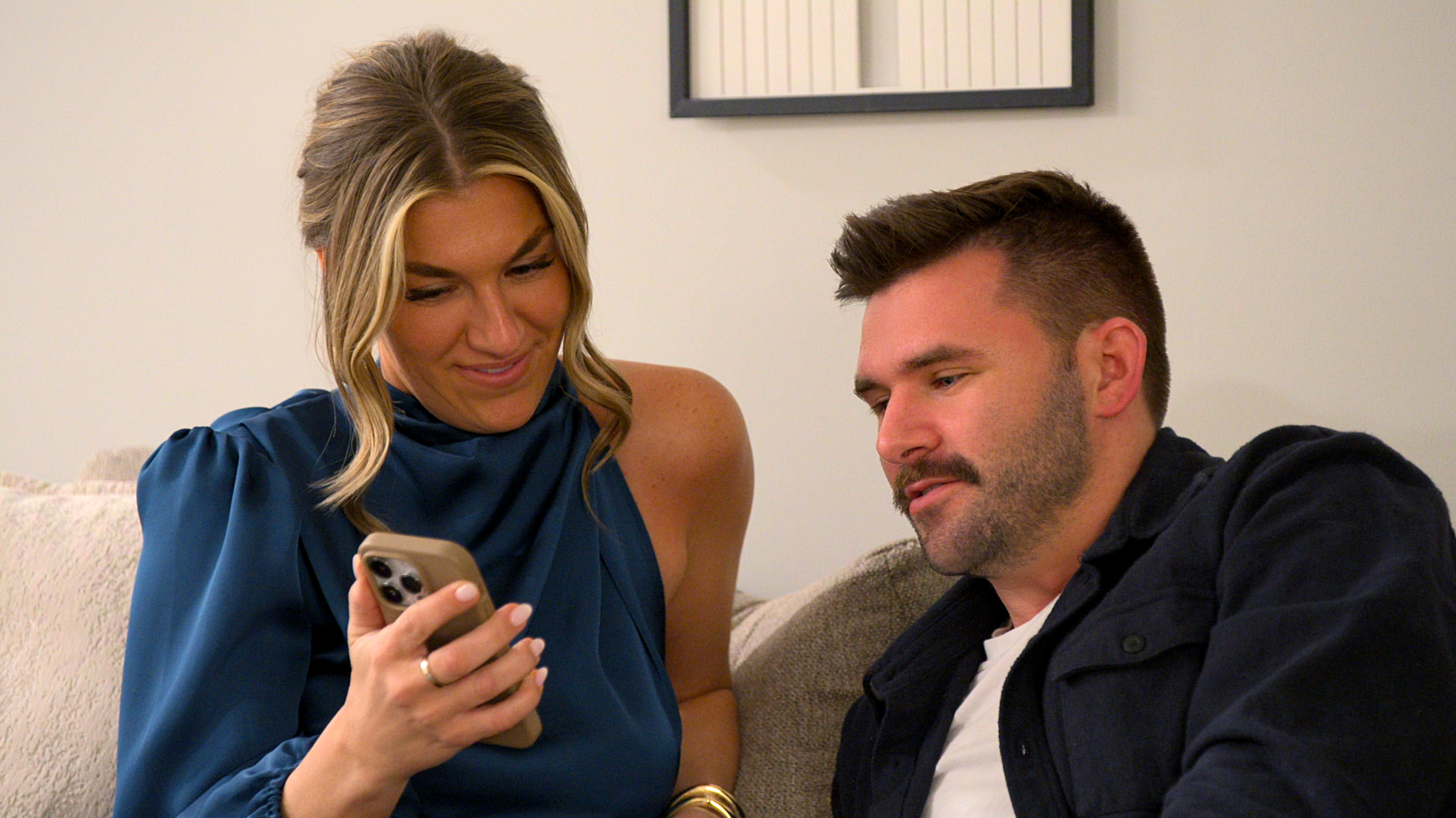 bri shows connor her phone while sitting on the couch together in a still from love is blind season 10
