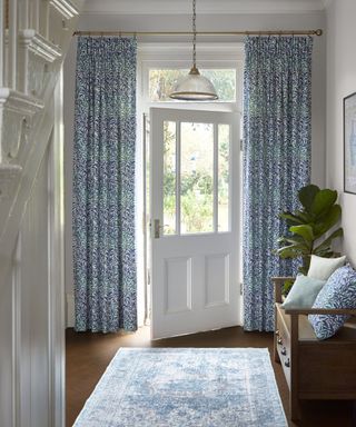 white entryway with blue door curtains, a blue rug and a wooden storage bench with drawers