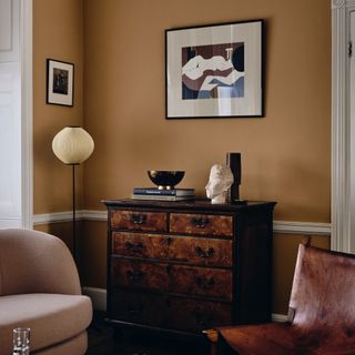living room paint colours 2023, ochre living room with artwork, vintage chest of drawers, blush sofa, floor lamp, leather chair
