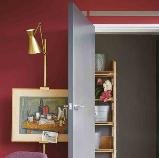 Maroon painted wall in room with grey door and golden folding light hanging over artwork