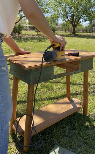 sanding down a wooden console table in a garden
