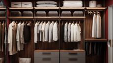 A wood closet with gray drawers, rails with shirts and t-shirts hanging on wooden hangers, shelves with storage boxes and pillows
