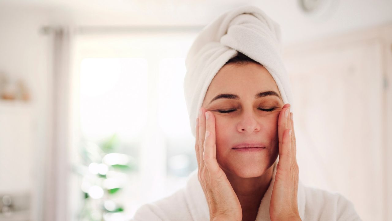 Portrait of mature woman in a bathroom at home applying moisturizer - stock photo