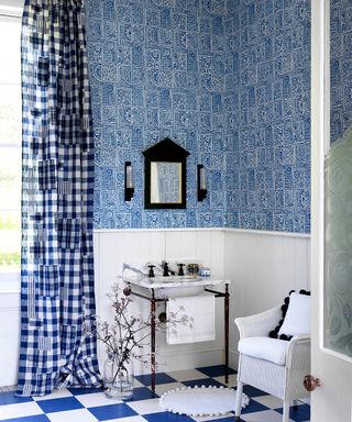 A blue and white bathroom with checkered flooring, gingham curtains and a white chair
