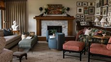 arts and crafts living room with a corner gallery wall, wooden and marble fireplace and eclectic furniture including a tapestry print couch, small blue tub chairs and pink accent chair with footstool