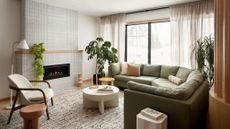 living room with white walls, rounded green sofa, and rounded tiled fireplace