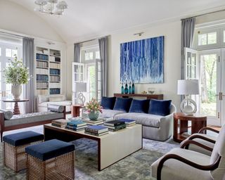 neutral living room with blue artwork, neutral sofas and chairs, gray chaise, blue cushions and stools and bookcase