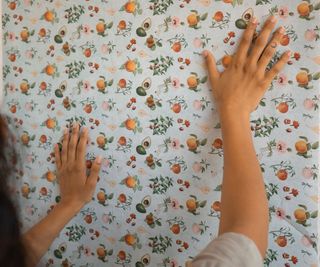 Woman's hands smoothing over fruit patterned wallpaper