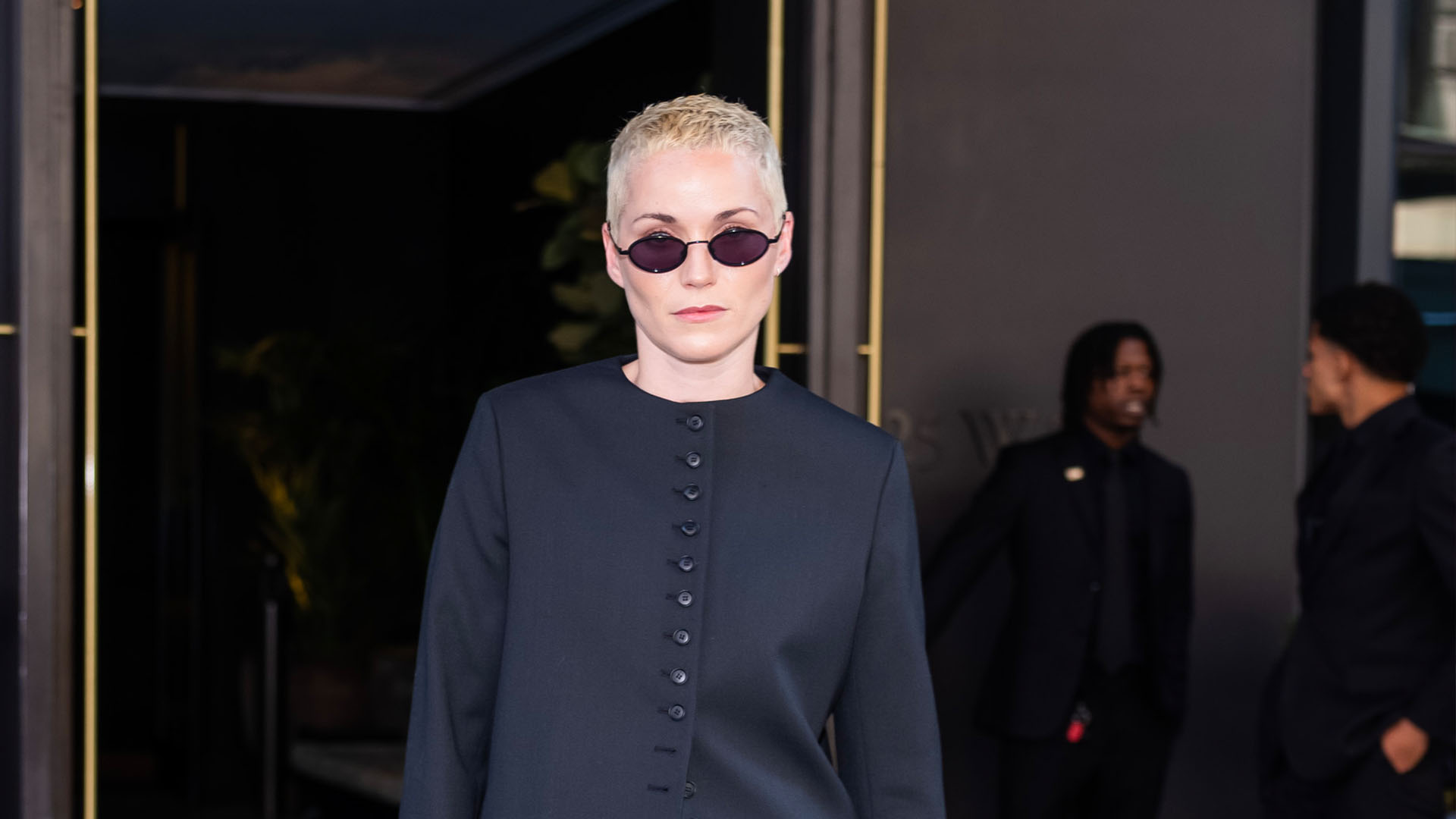 Jude Mack wearing a black blazer, blue jeans, and open-toe sandals