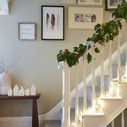 Ceramic light up houses on a side table next to a festive staircase.