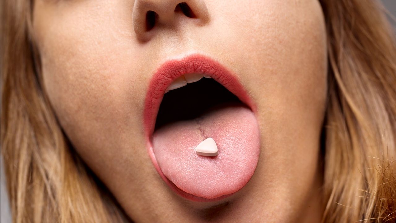 woman with mouth open and a pill on her tongue