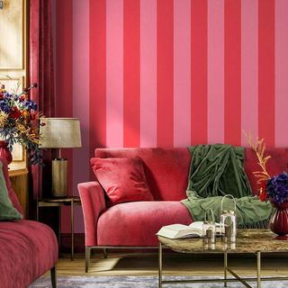 Pink and red strip wallpaper on a living room wall with a velvet sofa and coffee table in front of it