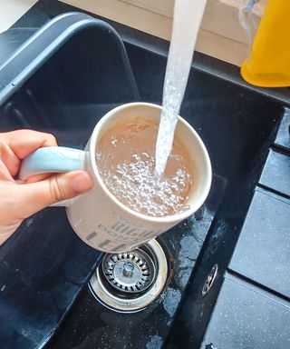 A black sink with a hand holding a white and blue mug with water being poured into it by a faucet