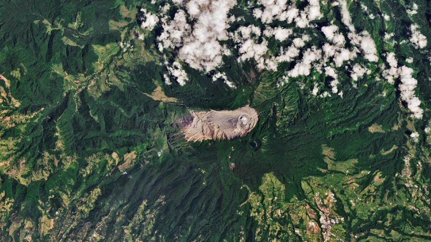A satellite photo of mountainous jungle with a barren, pale mountain situated in the center of the frame 