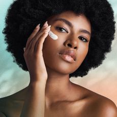 Black woman putting sunscreen on her cheek on blue and peach background