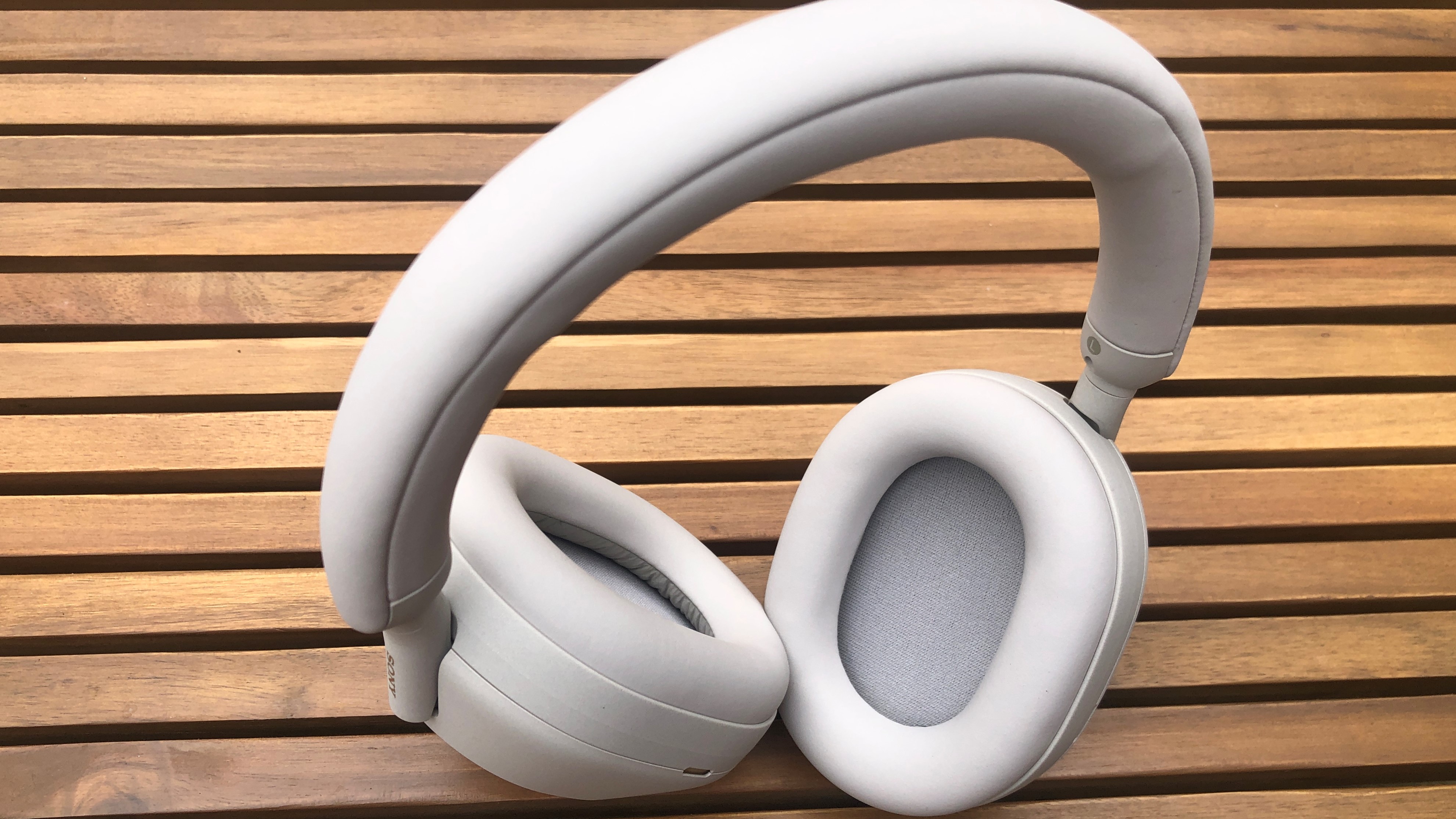 Sony XM5 headphones in ecru (off white) placed outdoors on a garden table