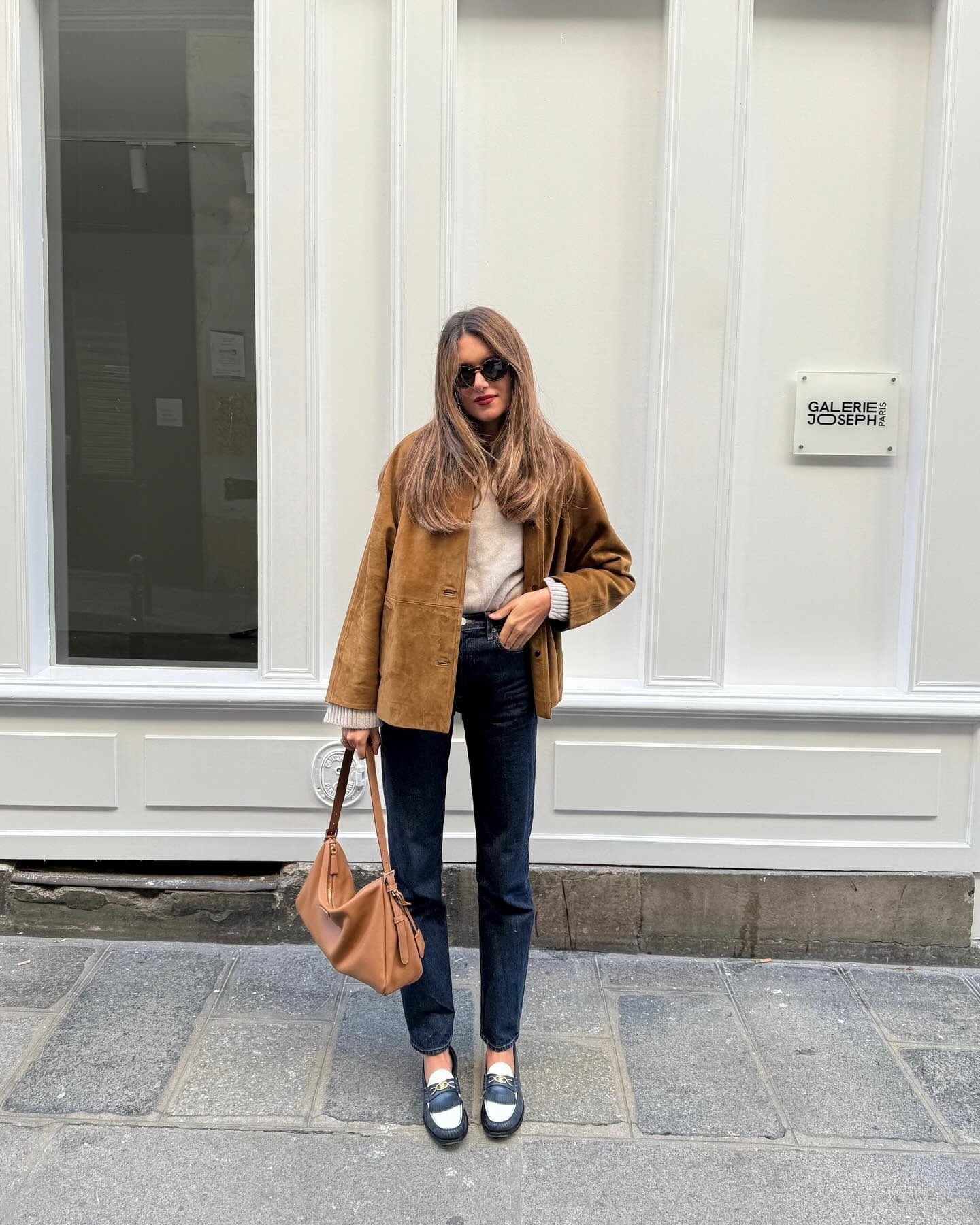 Fashion person wears the best autumn jacket in suede. She pairs her suede jacket with a cream shirt a black jean, white and black loafers and a brown slouchy bag. She is stood in front of a whit Joseph store looking directly into the camera in a recent image take from Instagram.