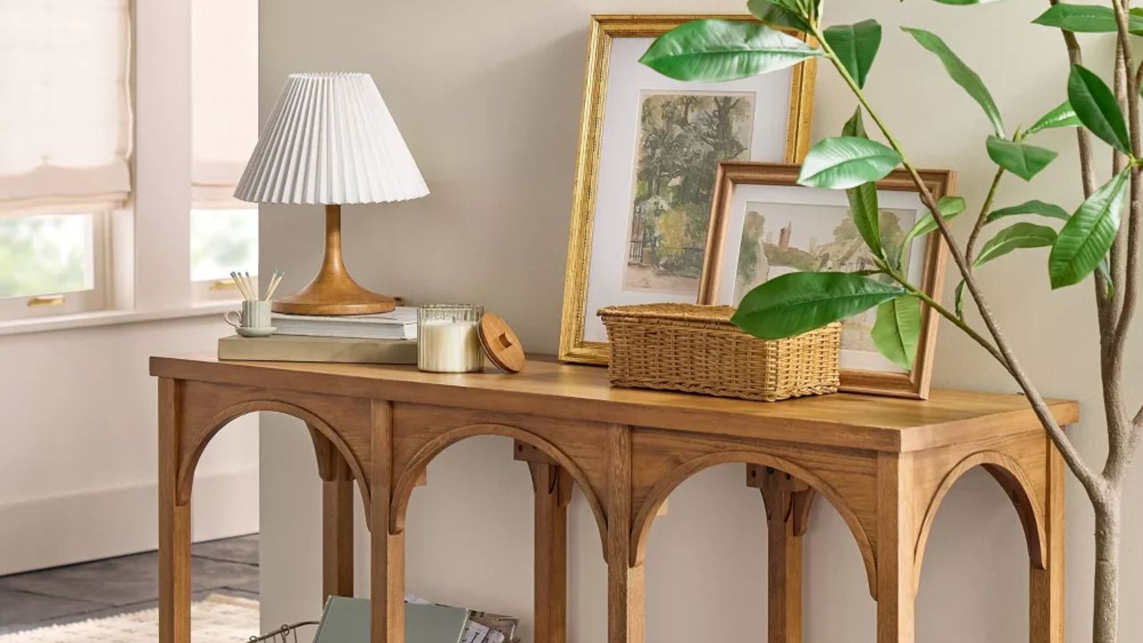 Entryway area featuring a wooden arched console table topped with a pleated shade table lamp, wicker basket, and assorted artwork