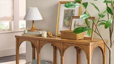 Entryway area featuring a wooden arched console table topped with a pleated shade table lamp, wicker basket, and assorted artwork