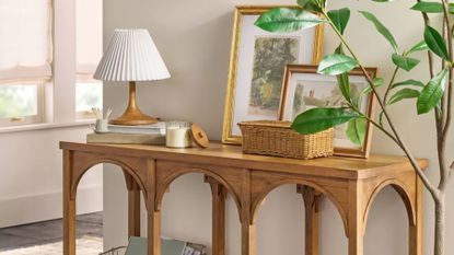 Entryway area featuring a wooden arched console table topped with a pleated shade table lamp, wicker basket, and assorted artwork