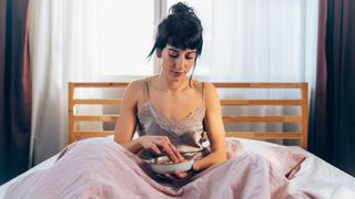 A woman sat crossed legged in bed holding a bowl of food