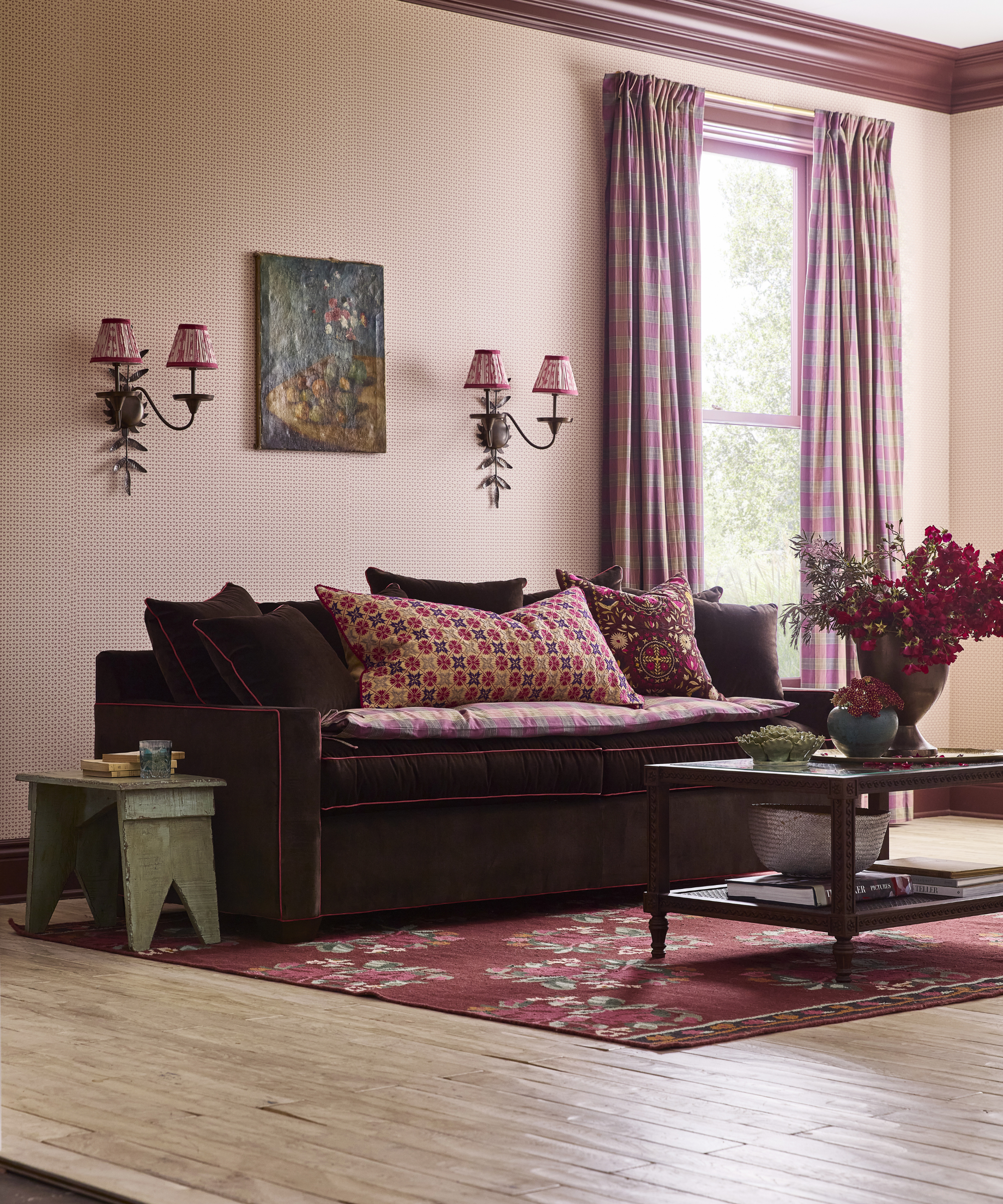 Moody pattern-drenched living room featuring a pair of double-shade wall sconces, tiny artwork, antique tables, and a dark purple sofa styled with floral and geometric throw pillows