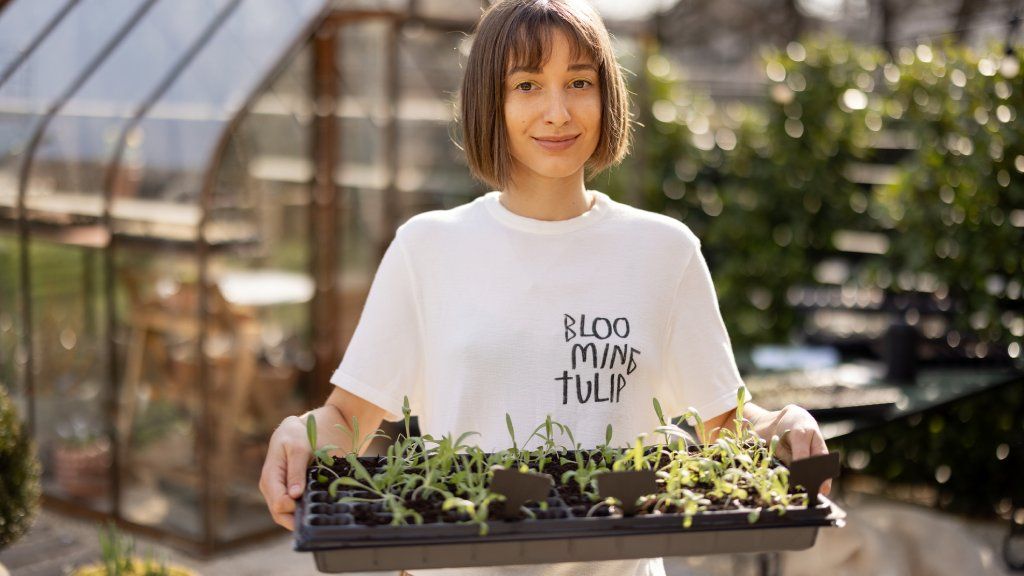 A young woman holds a tray of seedlings