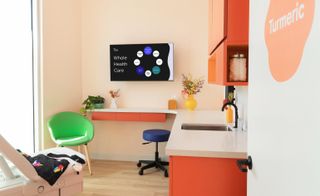 doctors office with examining bed, orange cupboards, green chair and tv on the wall