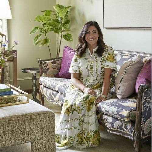 A woman in a green and white floral dress is sitting on a navy floral-patterned sofa in a light green living room.