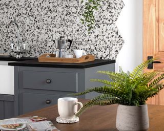 terrazzo tiles in kitchen with moka coffee machine, gray cabinets, and a wooden dining table with a plant, coffee mug and magazine