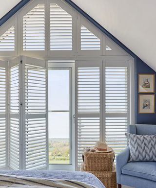 white bedroom with blue accents, blue armchair, large window with shutters