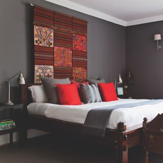 Grey bedroom with wooden bed and red patterned wall hanging