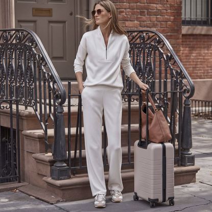 Woman in beige outfit set heading to airport with suitcase