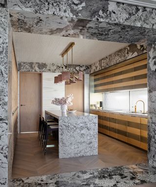 Luxurious kitchen by Greg Natale with a granite island, parquet floor and brass and wood striped cabinets