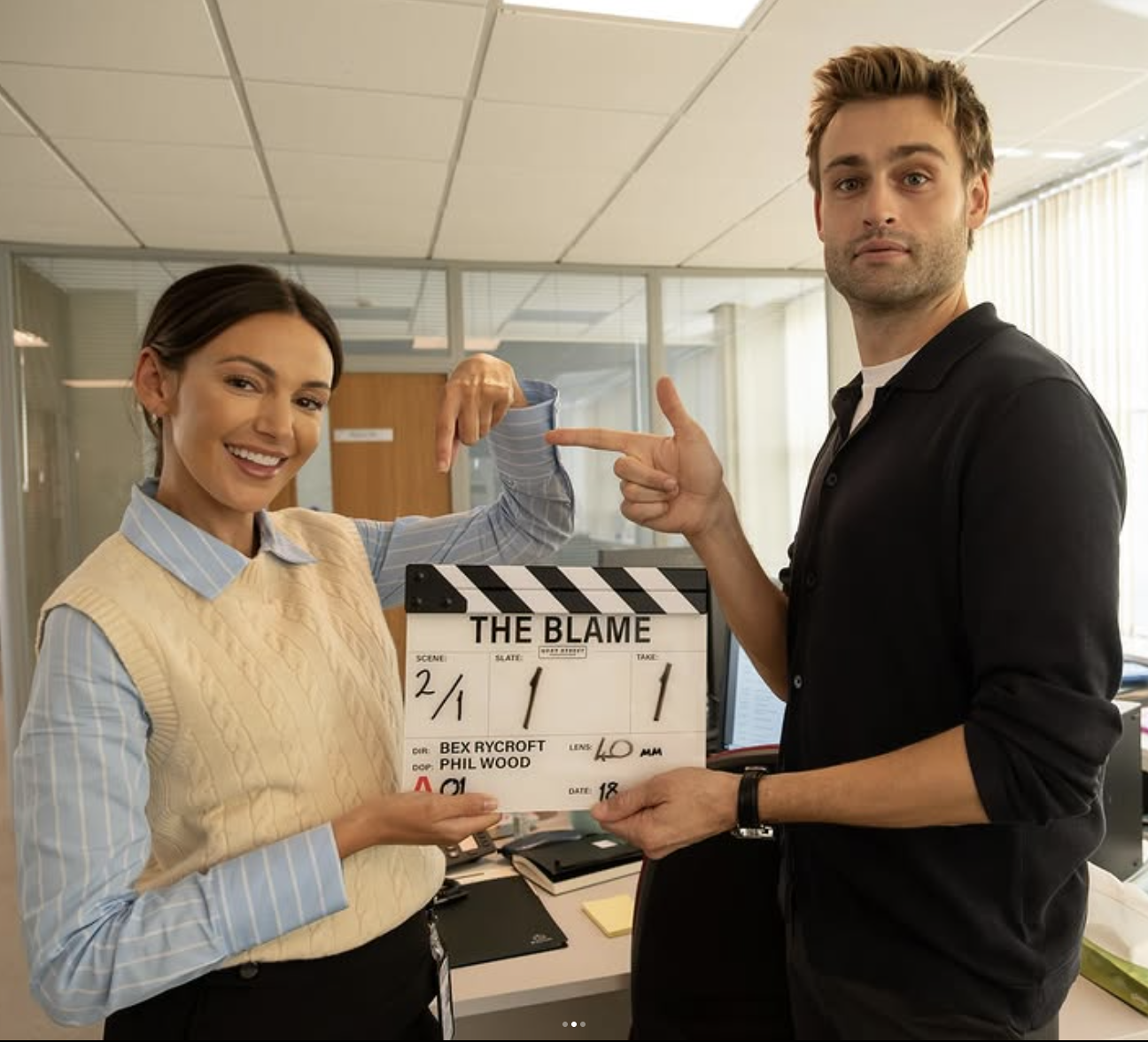 a BTS shot of Michelle Keegan and Douglas Booth on set for ITV's new drama The Blame, posing with a clapperboard