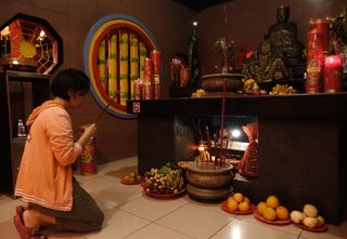 a woman kneels at an altar covered in fruit and red candles