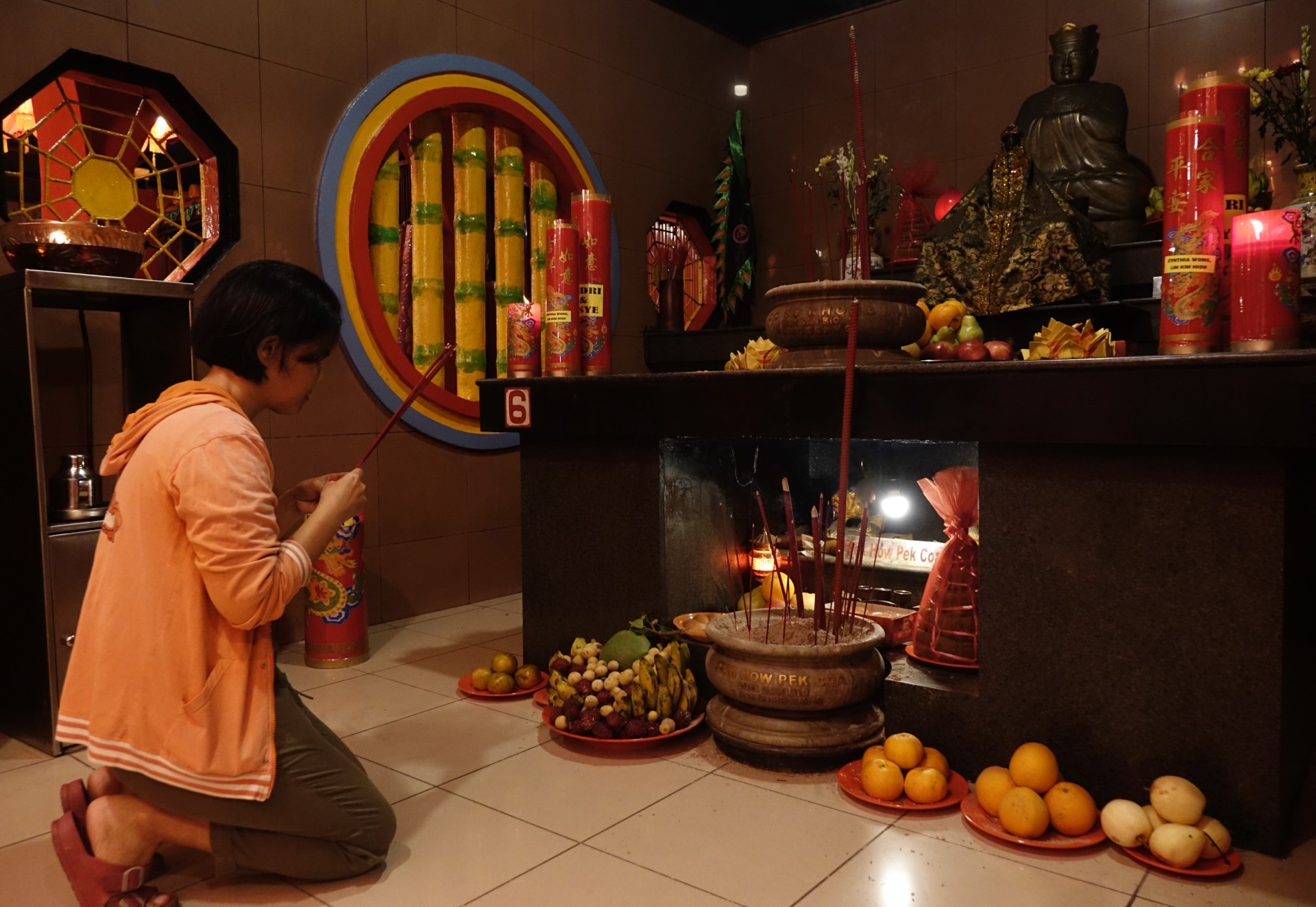 seorang wanita berlutut di depan altar yang dipenuhi buah-buahan dan lilin merah