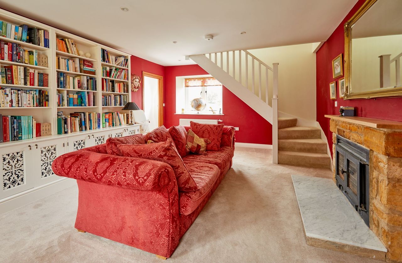 Sitting room with red sofa facing another fireplace, sitting opposite the stairs and a bookcase