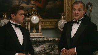 Allan Leech and Hugh Bonneville stand near the fireplace dressed in tuxedos in Downton Abbey: The Motion Picture.