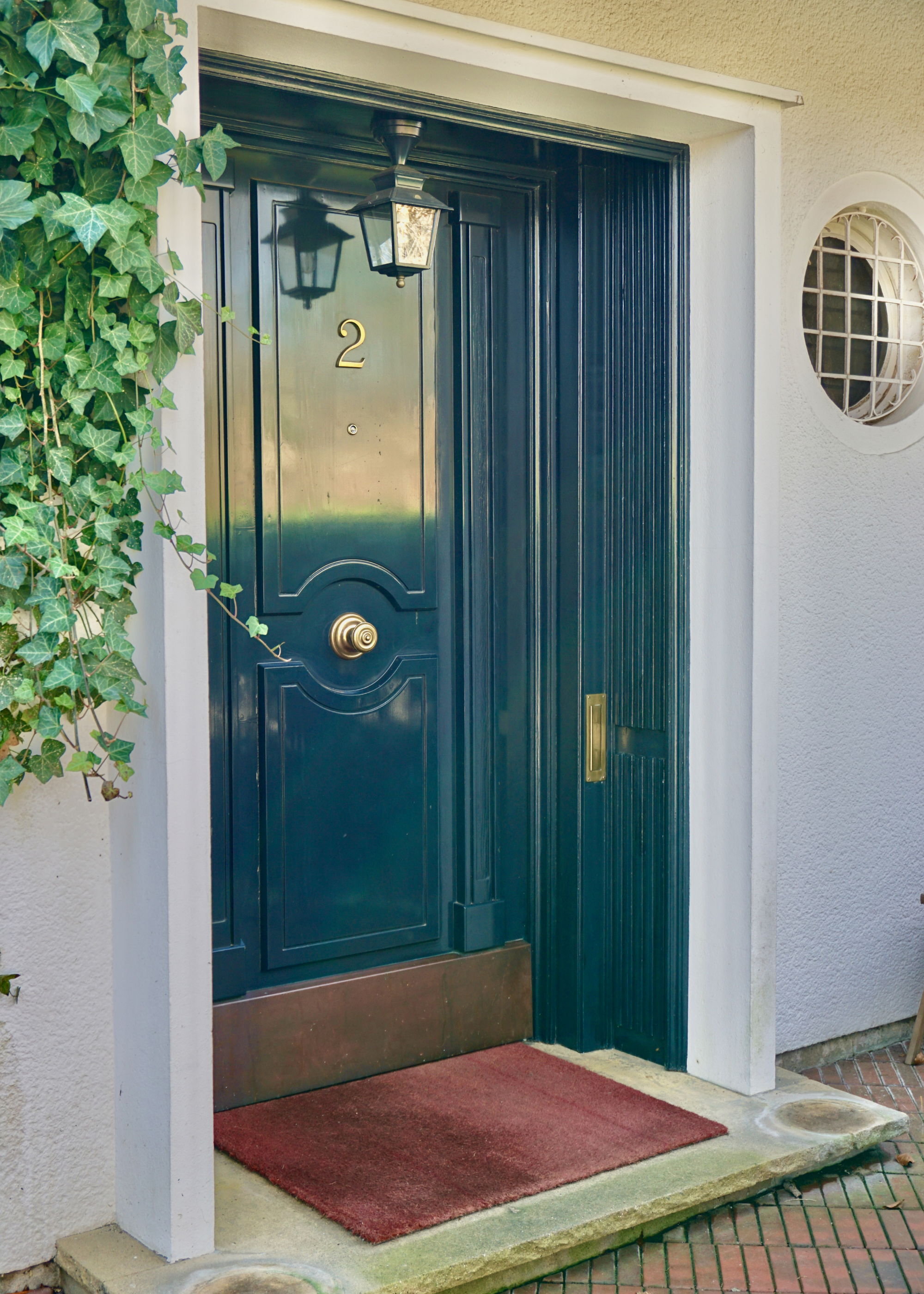 A front door and surround painted in Farrow &amp;amp; Ball's Railings with a lantern hanging from the center of the surround and ivy trailing down one side