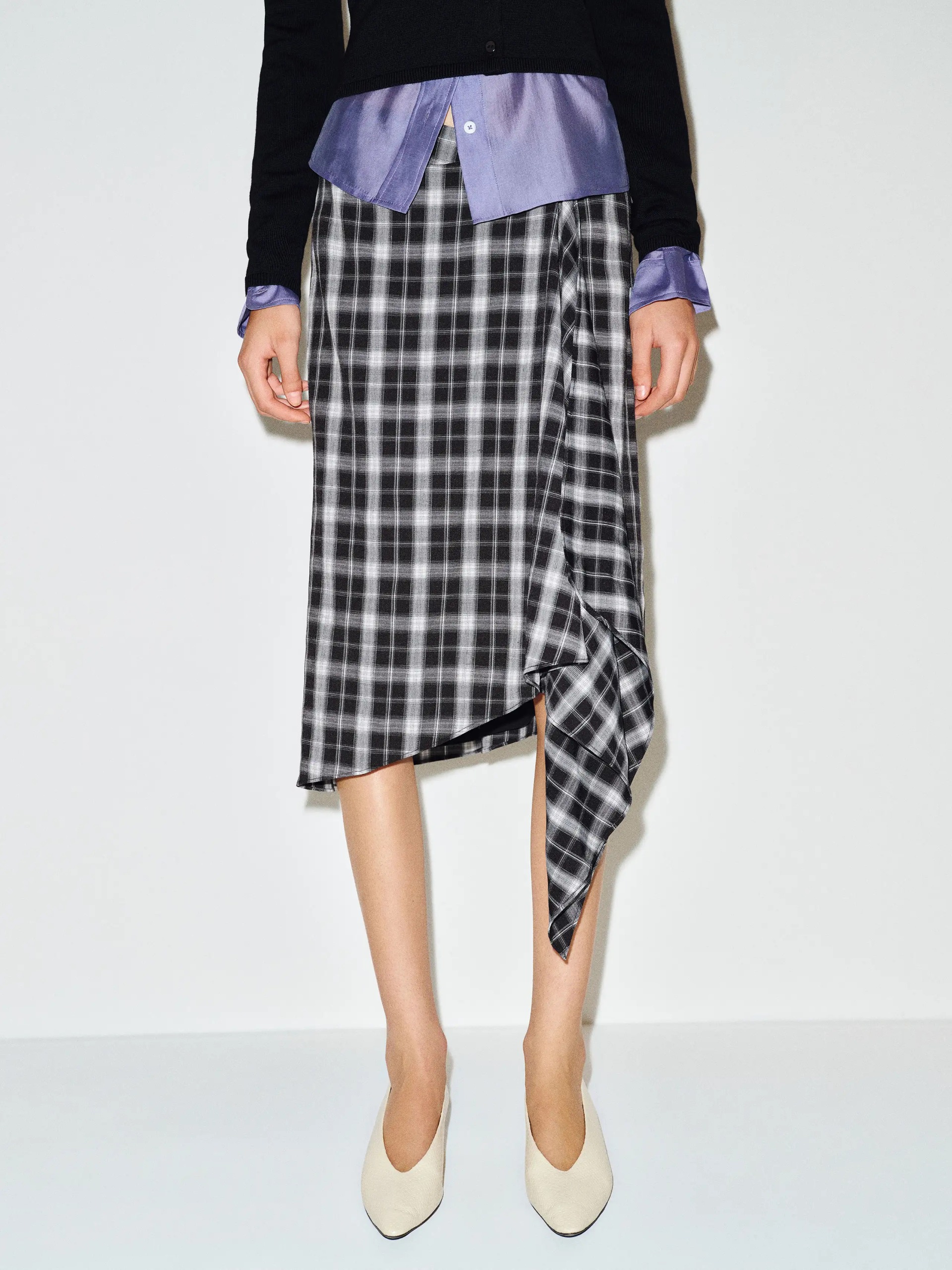 An image of a model wearing a plaid black and white skirt with white heels