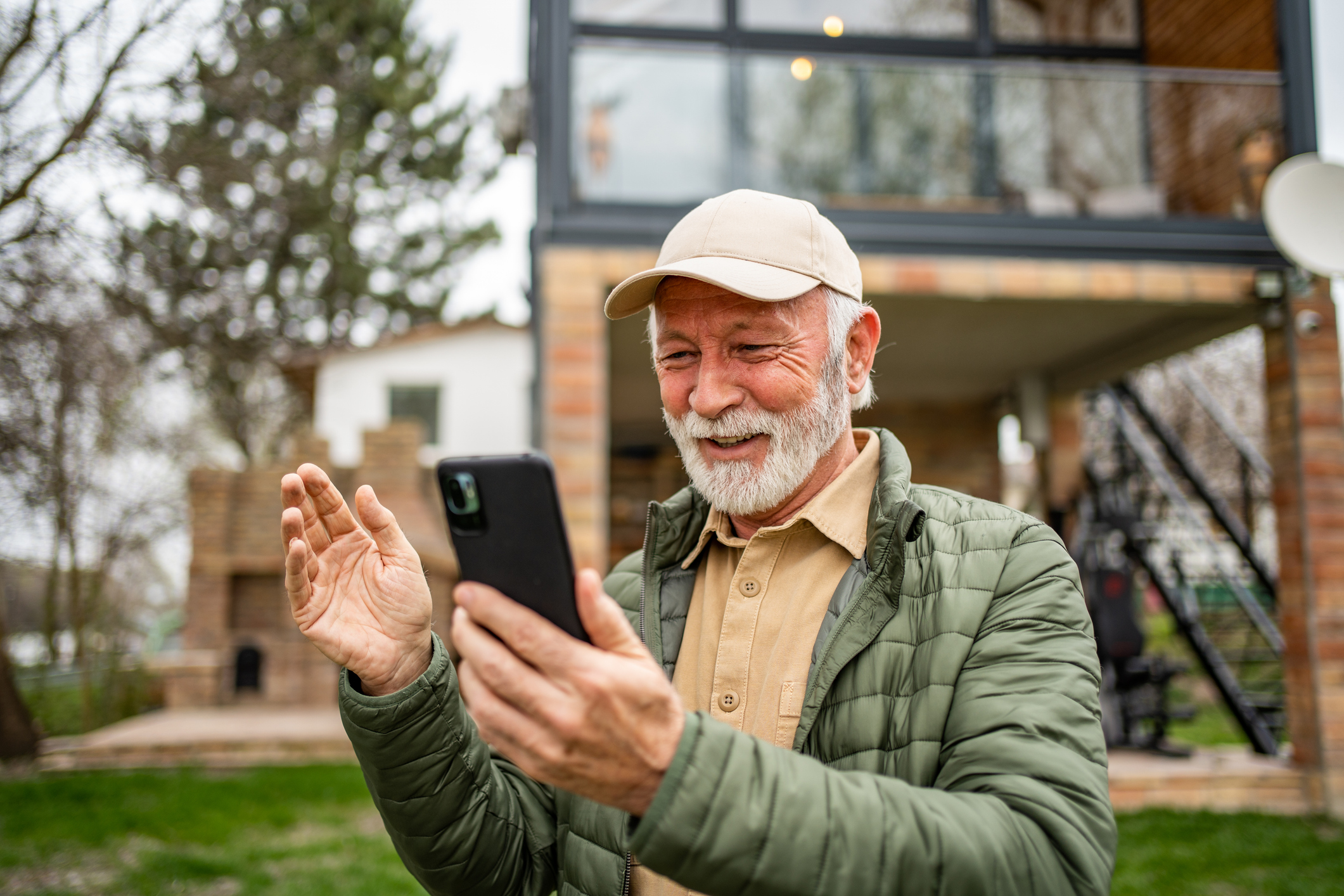 An elderly man stands in front of his cottage and uses a mobile phone to talk to his family