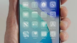 A hand holding an iPhone showing the 'all clear' look on iOS 26