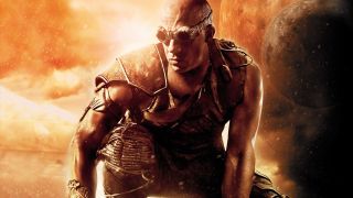 Still from the movie series The Chronicles of Riddick. Here we see Riddick crouching down. He’s a bald man wearing dark goggles and armor.