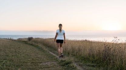 Woman walking along a path by the sea wearing shorts and t-shirt