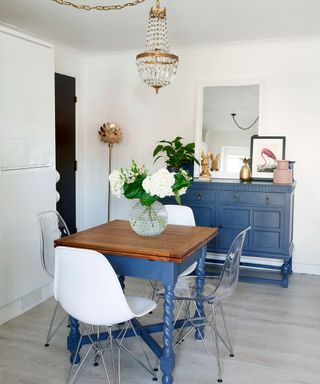 Blue painted sideboard and table with chairs in white room with chandelier
