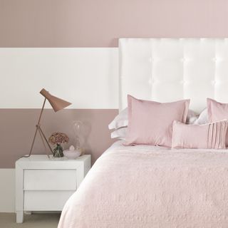 pink bedroom with pink and white striped painted wall with boutique hotel look with white upholstered bed and blush sit bedlinen