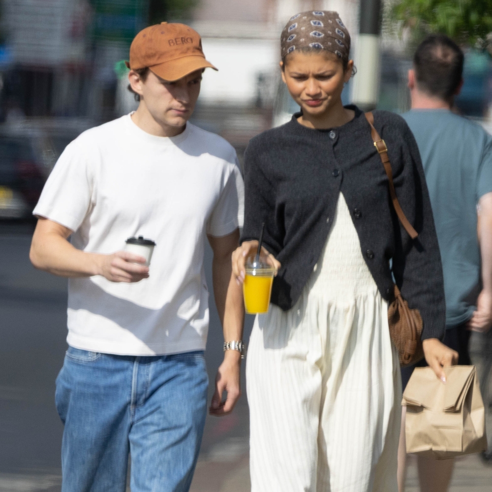 Zendaya walks down the street in London with Tom Holland wearing a white midi dress with a black cardigan, and brown bandana and brown Tabi ballet flats.