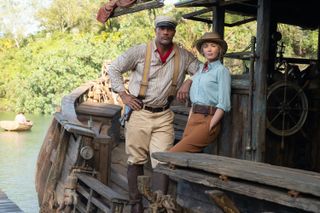 Frank (Dwayne Johnson) and Lily (Emily Blunt) stand on the deck of Frank's boat, both leading against the cabin as the river stretches out behind them