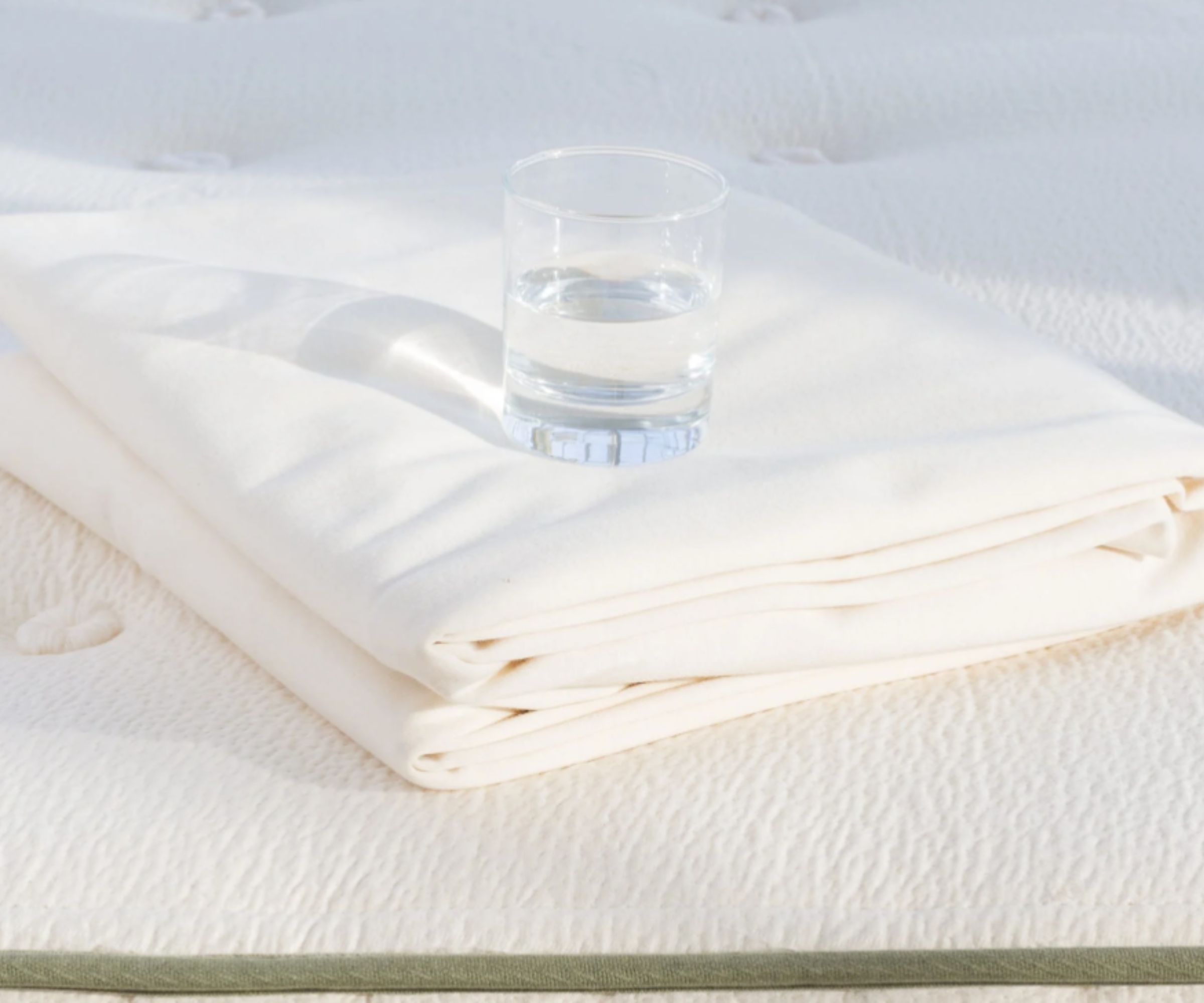 mattress protector folded on a mattress with a glass of water on top
